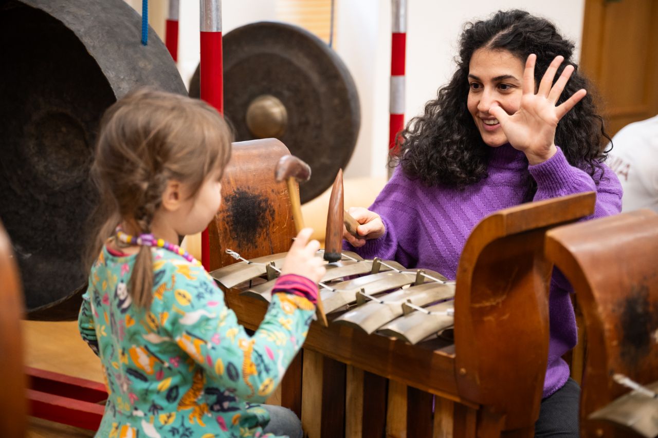 Ein Kind und eine erwachsene Frauen spielen zusammen ein balinesisches Orchesterinstrument. 